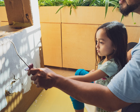 Painting cardboard with white paint and roller by a little girl.の写真素材