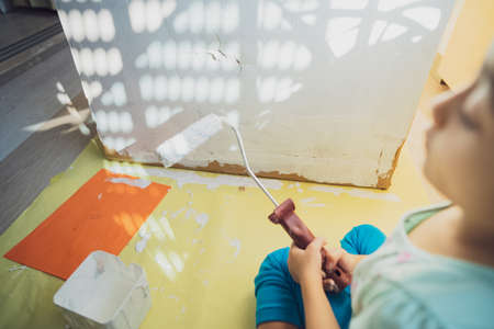 Painting cardboard with white paint and roller by a little girl.の写真素材