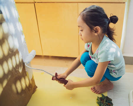Painting cardboard with white paint and roller by a little girl.の写真素材