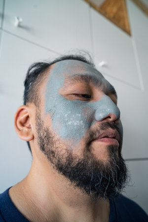 Beauty portrait of an excited matured Asian man standing isolated over white background, wearing facial cosmetic clay mask.の写真素材