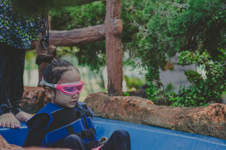 Little girl sitting on the slide in swimming pool. Wearing goggles and life jackets.の写真素材
