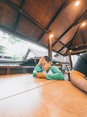 Young boy sitting at the table and using mobile phone. Looking strees and serious.