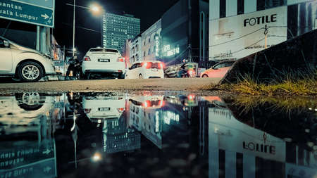 Kuala Terengganu, Malaysia - May 8, 2022 : Rainy night on the road with reflections. Close up view from the water puddle.のeditorial素材