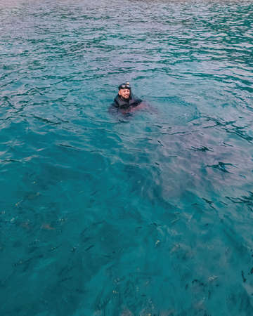 asian man wearing snorkel floating in open water surrounded by fishes.の写真素材