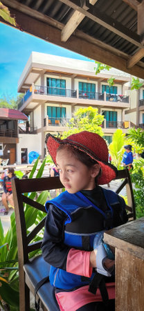 Adorable little girl wearing hat and life jacket sitting in a resort by the beach. Getting ready for the island hopping tour.の写真素材
