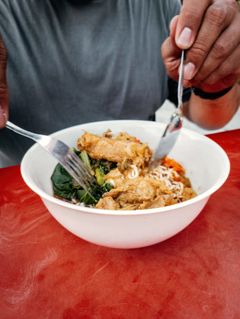 Eating Mee Ayam, Mie ayam, a noodles with chicken, meatballs, dumplings and vegetables is a popular street food in Indonesia.の写真素材