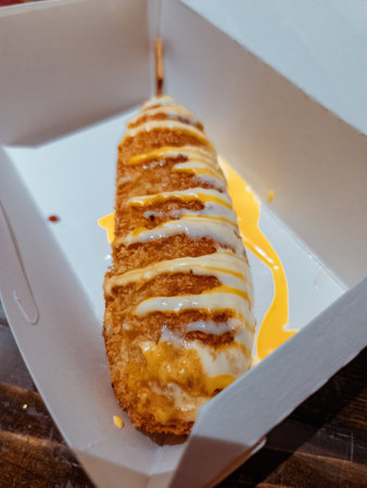 Korean Style Corn Dog Hatog drizzled with melted cheese in a take away box.の写真素材