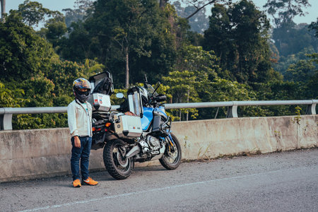 Pahang, Malaysia - Sept 24, 2022 Young boy wearing jacket standing next to the motorcycle at the roadside bridge.のeditorial素材