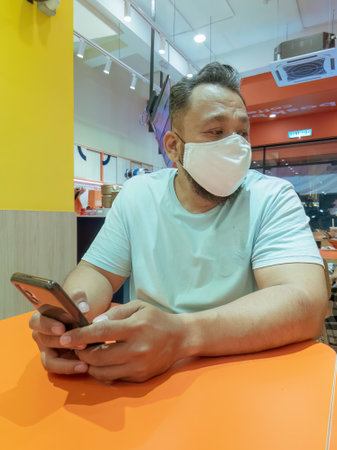 Matured man wearing face mask using mobile at the restaurant cafe. Low angle view.