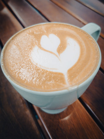 Love flower coffee,A cup of latte art with heart and flower pattern in a white cup on wooden backgroundの写真素材