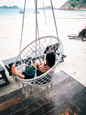 LIttle girl sitting on the beach swing or hammock and white sand and calm sea.のeditorial素材