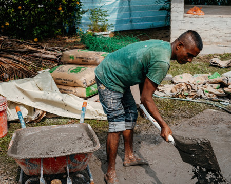 Selangor, Malaysia - October 21, 2023Man mixing concrete with shovel on the floor by hand at a house...