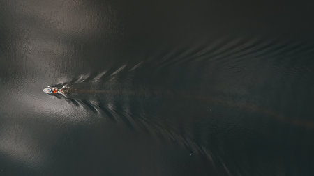 Top down, drone view of a boat sailing across the dark water of the lake.の写真素材