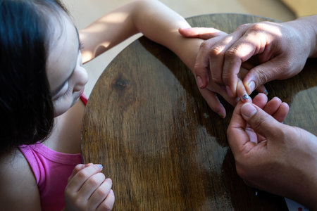 Adult hand placing colourful nail stickers to the little girl's hand. .の写真素材