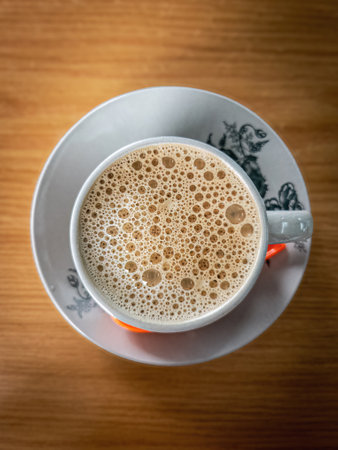 Top view of bubbles on the white coffee served in Kopitiam cup on the wooden table.の写真素材