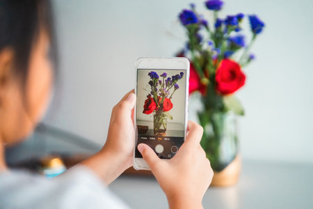 Taking photo with a mobile phone of a bouquet of fresh roses with baby breath at home.の写真素材
