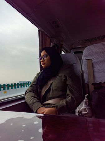 Teenager wearing hijab and glasses sitting on the bus looking out through the window. Travelling concept.の写真素材