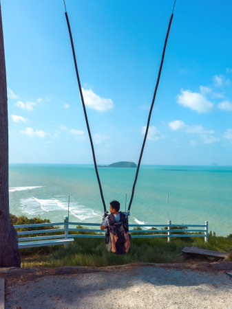 A boy is on a giant swing against the sea background.  Viewed from behind.の写真素材