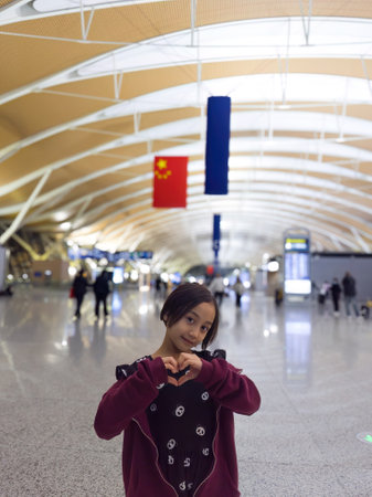 Little girl with heart shaped hand sign at the China Airport. Travelling concept.の写真素材