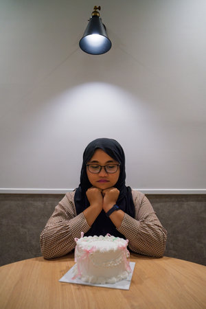 Asian muslim teenage girl wearing glasses with a vintage birthday cake sitting on the table.の写真素材
