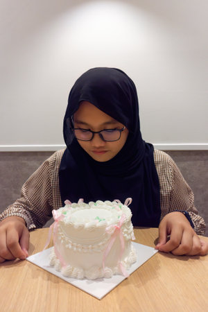 Asian muslim teenage girl wearing glasses with a vintage birthday cake sitting on the table.の写真素材