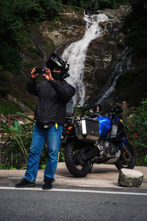 Perak, Malaysia - September 15, 2022 A biker wearing helmet is taking photo at the Lata Kinjang waterfall near his motorcycle.の写真素材