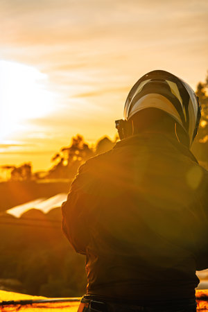 Moody orange sunrise with a silhouette of a motorcycle rider with helmet from behind.の写真素材