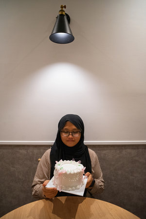 Asian teenage girl wearing glasses with a birthday cake sitting on the table.の写真素材