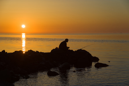 Silhouette of fisherman at dawn. Orange serene and quiet sea.の写真素材