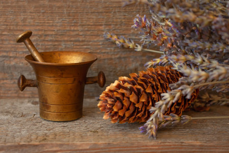 Ancient still life on a wooden table, nostalgic theme. Old bronze mortar and pestle, dry lavender and pine cone. Image for cover or wallpaper.の写真素材