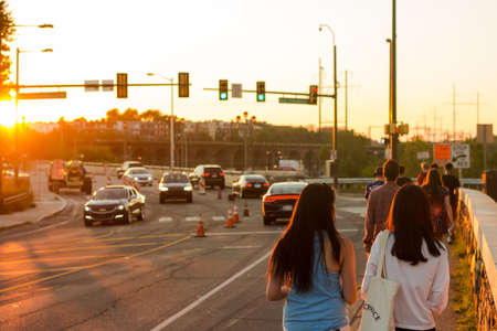 People walk along a road in the city, with traffic and the setting sunのeditorial素材