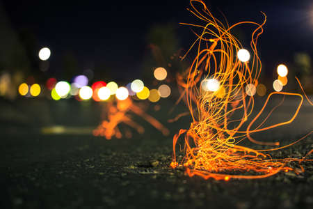 A long exposure of a cigarette being flicked, with colorful lights in the backgroundの写真素材
