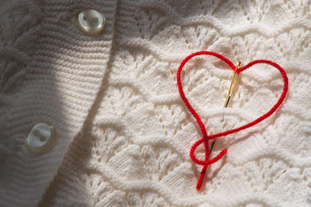 The red thread in the needle in the shape of a heart on a white blouseの写真素材