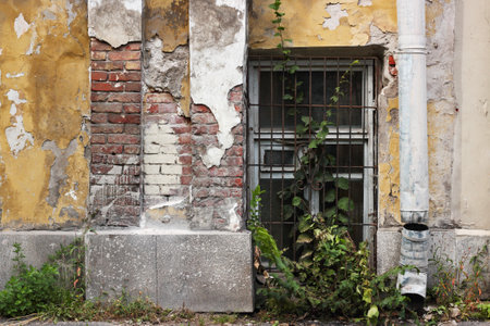An old brick building with peeling off paint and a basement window with a latticeの写真素材