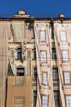 Repair-construction work of the facade of an old building at an altitude near the roof