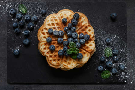 Soft Viennese waffles with blueberries sprinkled with icing sugar Top view, close-up on a dark concrete backgroundの写真素材