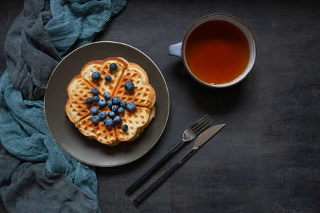 Soft Viennese waffles with blueberries and cup of tea. Top view, close-up on a dark concrete backgroundの写真素材