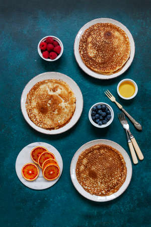 Delicious homemade pancakes with raspberries, blueberries, honey and bloody orange fruit on classic...