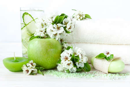 Blossoming apple tree flowers, cold drink, green apple, aromatic sea salt, candle and towels. Concept for spa, beauty and health salons. Close up photo on white wooden background, selective focusの写真素材