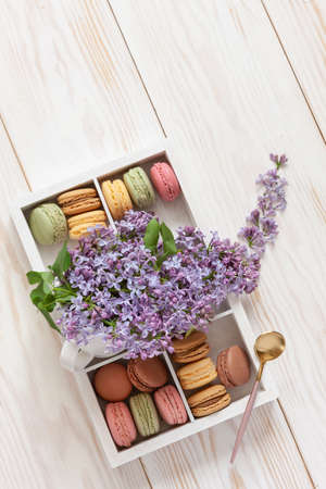 Bouquet of fresh fragrant lilac in white cup and delicious macaroons cookies in box on  white wooden background.の写真素材