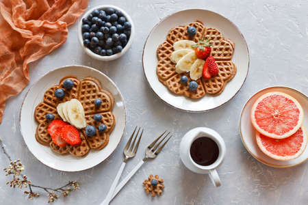 Pieces of homemade waffle cake with banana and blueberries on the plates on gray background