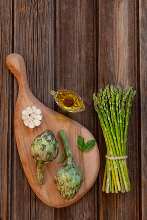 Top view of fresh artichoke and Bunch of green asparagus with garlic and olive oil on wooden tableの写真素材