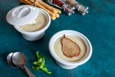 Vegetarian celery root homemade cream-soup with blue cheese, fresh caramelized pear and breadsticks. Close up, top view on the blue backgroundの写真素材