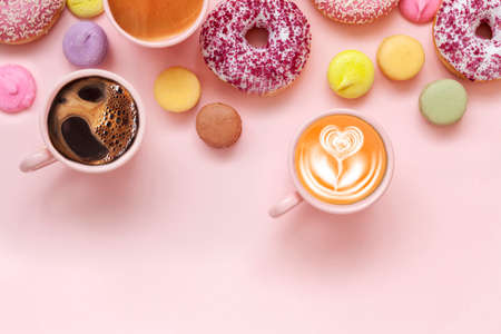 Coffee cups, delicious pink donuts with sprinkle and colorful bright macaroons on pink paper backgroundの写真素材