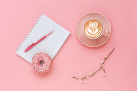 Latte Coffee cup, delicious pink donut with sprinkle, notebook for notes and pen on pink paper backgroundの写真素材