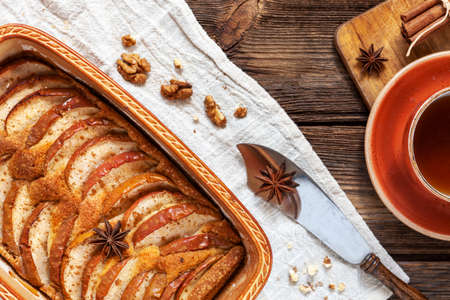 Apple pie, cup of fragrant tea, cinnamon sticks, anise and cutting knife in rustic style on a wooden backgroundの写真素材