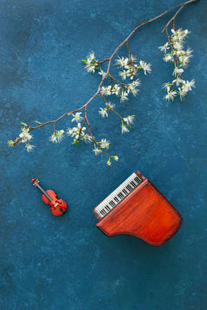 Miniature copies of the piano and violin with blossoming cherry tree branches. Top view, close-up on classic blue backgroundの写真素材