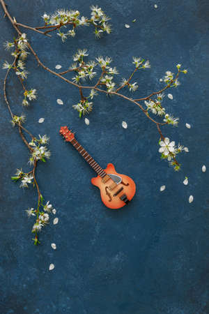 A miniature copy of a guitar and flowering cherry branches on a classic blue background, top viewの写真素材