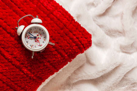 Close up of a red pillow and alarm clock on white blanket backgroundの写真素材