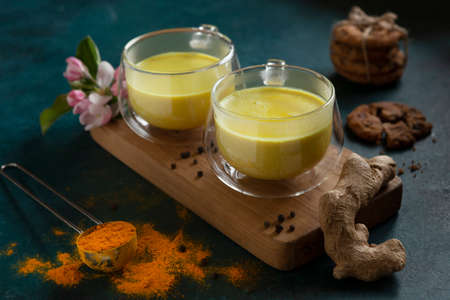 Two cups of ayurvedic drink golden milk turmeric latte with curcuma powder, ginger and honey over...
